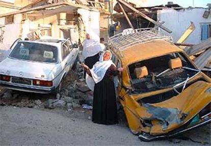 Unas mujeres lloran delante de los coches y viviendas que fueron alcanzados por el fuego israelí en el campo de refugiados de Rafá, en Gaza.