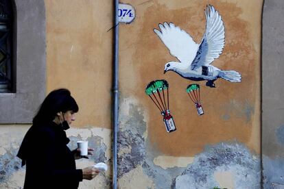 Una mujer pasa por delante de un mural que representa una paloma blanca lanzando en paracaídas viales de la vacuna contra la covid-19, cerca de la sede del Ministerio de Sanidad italiano en Roma.