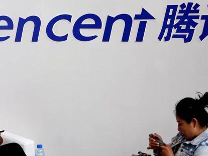 Dos mujeres juegan en su telefono móvil bajo un cartel de la empresa Tencent.