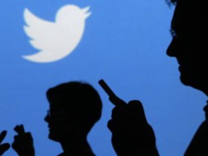 Gente con móviles en sus manos delante del logo de Twitter.