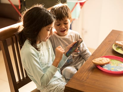 Dos niños se entretienen con un móvil mientras desayunan.