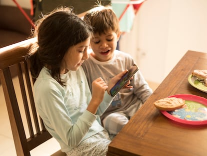 Dos niños se entretienen con un móvil mientras desayunan.