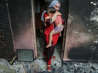 Una mujer lleva a su hijo en brazos en su casa quemada, tras un incendio forestal en Bejaia (Argelia).