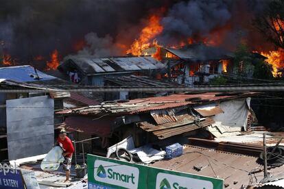 Una mujer rescata algunas de sus pertenencias ante el temor de que las llamas lleguen a su casa durante un incendio declarado en una barrio de chabolas en el distrito de Pasong Tamo, en el este de Manila (Filipinas).