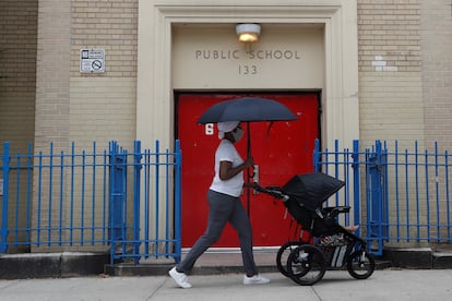 Una mujer camina frente a una escuela pública con su bebé, en Nueva York.