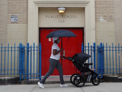 Una mujer camina frente a una escuela pública con su bebé, en Nueva York.