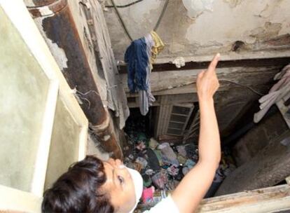 Una vecina, protegida con una mascarilla, señala la basura acumulada en el patio interior del edificio de Málaga donde vive.