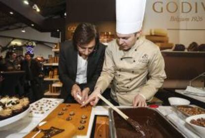 El primer ministro belga, Elio Di Rupo (i), hace unos bombones en el "estand" de Godiva en la Feria del Chocolate en Bruselas, Bélgica.