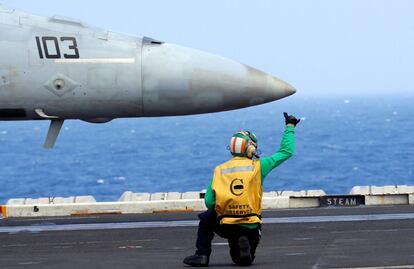 Un miembro de la tripulación de la cubierta señaliza al piloto de un caza de combate F18 que se encuentra situado en la cubierta del portaviones USS Carl Vinson.