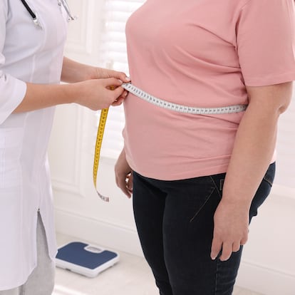 Nutritionist measuring overweight woman's waist with tape in clinic, closeup