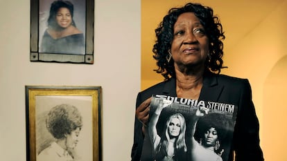 Dorothy Pitman Hughes poses in her St. Johns, Fla., home on Sept. 24, 2013, with a poster using a 1970's image of herself and Gloria Steinem. Hughes, a pioneering Black feminist, child welfare advocate and activist who formed a powerful speaking partnership with Steinem and appeared with her in one of the most iconic photos of the feminist movement, has died. Hughes died Dec. 1, 2022, in Tampa, Fla. She was 84. (Bob Self/The Florida Times-Union via AP)