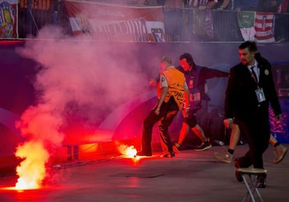 Un miembro de la seguridad privada del Atlético y un operario tratan de apagar una de las bengalas lazandas por los aficionados del Benfica