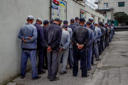 Los reos aguardan en fila a recibir una orden para marchar hacia el comedor. El pasillo en el que están tiene carteles a ambos lados con imágenes de héroes y personalidades históricas de Ucrania.