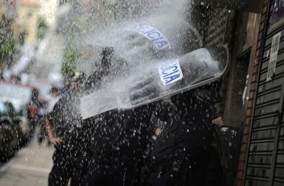Agentes de la policía se cubren con sus escudos del agua que les arrojan los activistas desde el balcón.