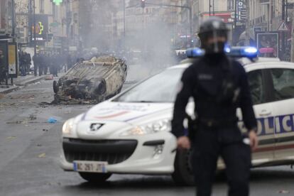 Un oficial de policía permanece frente a un automóvil incendiado por estudiantes durante una protesta contra las reformas educativas del gobierno francés, en el norte del suburbio de Aubervilliers, en París.