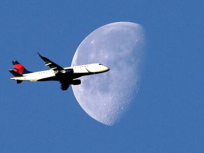 Un avión cruza el cielo ante la luna.