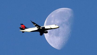 Un avión cruza el cielo ante la luna.
