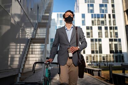 EXTRA ESCUELA DE NEGOCIOS 24-04-22 Low angle view of a young businessman with a protective face mask going to the office with a bicycle