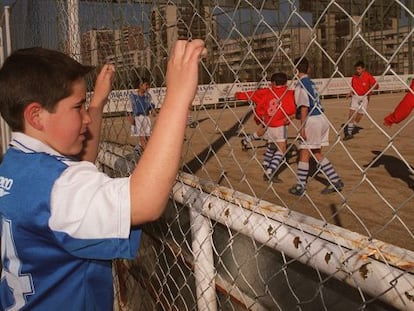 Un niño observa desde la verja como juegan sus compañeros.