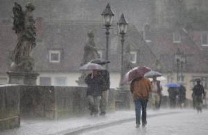 Varios personas caminan por una calle bajo una intensa lluvia, en Wuerzburgo (Alemania). EFE/Archivo