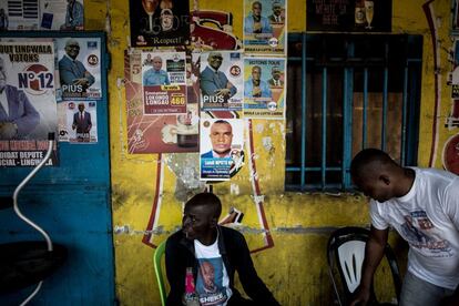 Un hombre sentado en la fachada de un bar, cubierta con carteles electorales, en el distrito de Lingwala (República Democrática del Congo).