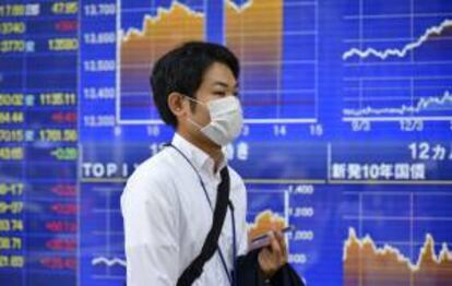 Un hombre camina junto a una pantalla informativa en la que aparece información bursátil en Tokio (Japón). EFE/Archivo