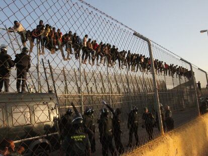Un grupo de inmigrantes permanecen encaramados a la valla de Melilla, mientras efectivos de la Guardia Civil les esperan en el suelo, el pasado 23 de enero.