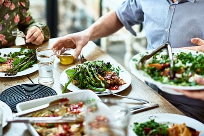 Varias personas se sirven ensalada alrededor de una mesa.