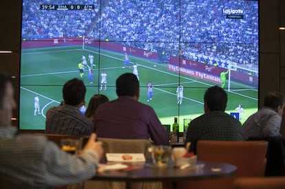 Varios clientes ven un partido de fútbol en un bar.