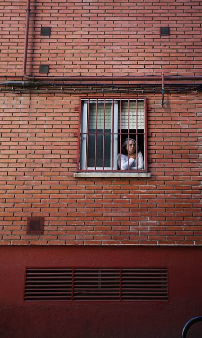 Una vecina del barrio mira por la ventana de su casa todo lo que sucede en el intento de desalojo de la vivienda de la calle Alfalfa 41.