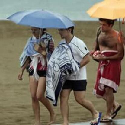 Cuatro jovenes abandonan protegidos por paraguas la playa de la Malvarrosa, en Valencia