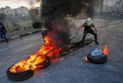 Un manifestante palestino usa un palo para mover unas ruedas ardiendo durante los enfrentamientos con las fuerzas de seguridad israelíes cerca del puesto de control de Qalandia, en Cisjordania.