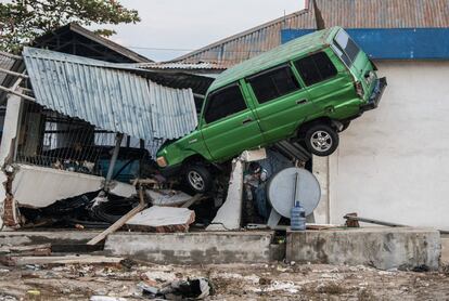 Un hombre se encuentra debajo de un automóvil que ha sido arrastrado hasta un edificio, en Palu.