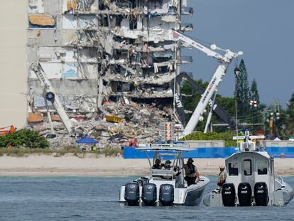 Botes de la policía de Miami vigilan a lo lejos los restos del edificio colapsado, en Surfside