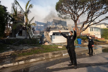 Un par de policías piden paso para una patrulla de bomberos que llega a una vivienda incendiada en Pacific Palisades, en Los Ángeles, California.