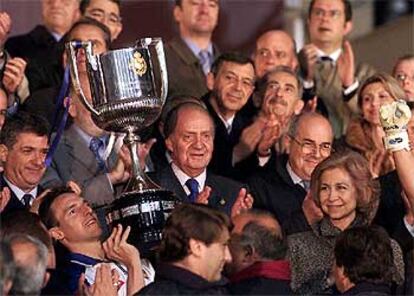 Cuartero levanta el trofeo tras recibirlo del Rey, que aplaude junto la Reina y demás autoridades.