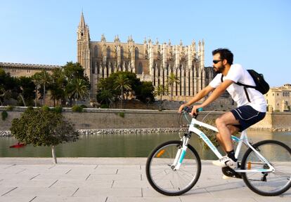 Un joven circula con su bicicleta junto a la catedral de Palma.