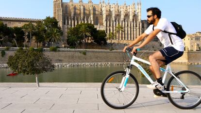 Un joven circula con su bicicleta junto a la catedral de Palma.