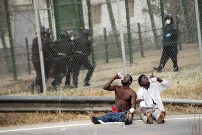 Las fuerzas de seguridad trasladan a un inmigrante en el interior de la verja, mientras otros dos beben agua al otro lado de la valla.