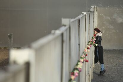 Una joven mira por una rendija del muro en la Bernauer Strasse que se ha llenado de flores para conmemorar los 26 años que han pasado desde la caída.