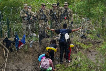 A migrant, looking to cross in the U.S., holds out his arms while appealing to Texas National Guardsmen