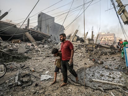 Un hombre camina con su hijo sobre los escombros producidos por un bombardeo israelí sobre Gaza.