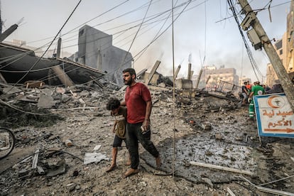 Un hombre camina con su hijo sobre los escombros producidos por un bombardeo israelí sobre Gaza.