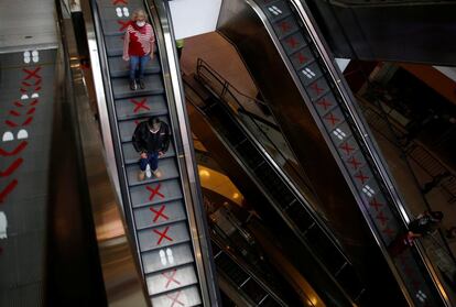 Los clientes bajan por una escalera mecánica con señales que indican la distancia de seguridad que deben guardar, en un centro comercial de Lima (Perú).