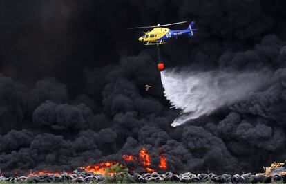Un milano negro escapa de las llamas mientras un helicóptero intenta controlar el incendio del cementerio de neumáticos de Seseña (Toledo), el 14 de mayo de 2016. El incendio tardó tres semanas en ser extinguido definitivamente.
