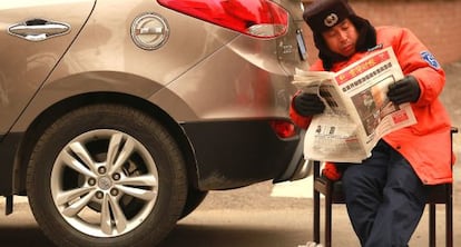 Un aparcacoches lee un periódico junto a un vehículo en Pekín.