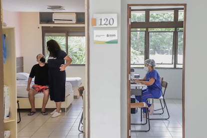 Luciano e a esposa, Jéssica, na suíte onde estão acomodados. Ao lado, uma profissional de saúde trabalha.