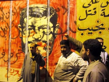 Tres personas frente a un mural que muestra al presidente egipcio Mohamed Morsi.