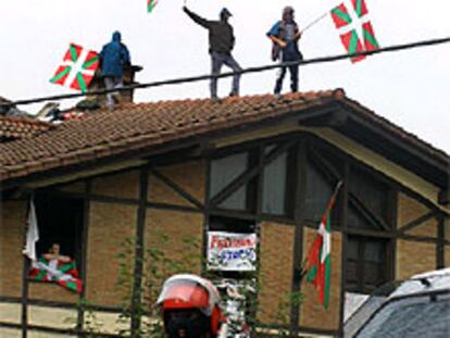 Un <i>ertzaina</i> vigila la <i>herriko taberna</i> de Durango, mientras partidarios de Batasuna permanecen en el tejado portando <i>ikurriñas.</i>