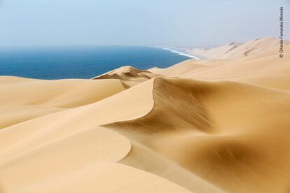 Alto de una duna en la costa desértica de Namibia, donde los montículos de arena esculpida por el viento se funden con las olas del Atlántico que se estrellan.